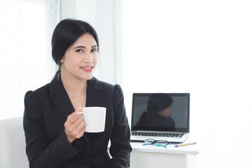 Beautiful asian businesswoman in black suit sitting and holding a cup of coffee