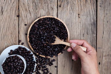 Wall Mural - hand holding wooden spoon with coffee beans on old wooden plank background.