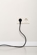 Black power cord cable plugged into european wall outlet on white plaster wall