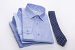 Three blue men's shirts folded in a pack and tie on a white background.