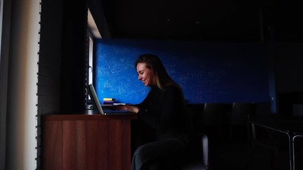 Wall Mural - Young woman specialist in IT technologies prints on laptop keyboard and creates new application sitting in office at wooden table on winter day. Beautiful European-looking woman with long blond hair