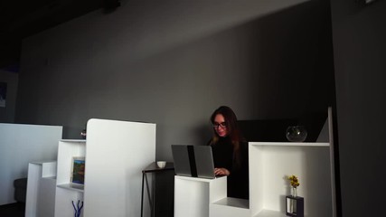 Wall Mural - Successful girl wears glasses and includes computer for work, collects and analyzes various information, sits at desk in office of modern office. Beautiful European-looking woman with long blond hair