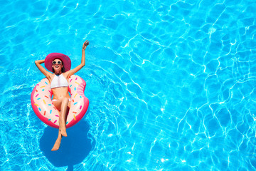 Wall Mural - Beautiful young woman relaxing on inflatable donut in blue swimming pool