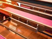 Back Of Pew With Bookshelf In Empty Church. Cathedral Interior With Wooden Long Bench