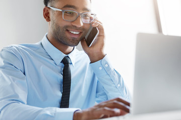 Wall Mural - Young owner of company calling financial manager, having happy look in his notebook, being glad to see big profits of his company. Businessman signing new contract with his parter over mobile phone