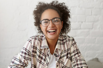 Happy female with dark pure skin and crisped hair wearing elegant glasses and shirt smiling sincerely into camera. Mixed race cute female student being glad to pass all her exams successfully