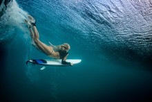 Blonde Girl Surfer Holding White Surf Board Diving Duckdive Under Big Beautiful Ocean Wave. Turbulent Tube With Air Bubbles And Tracks After Sea Wave Crashing.