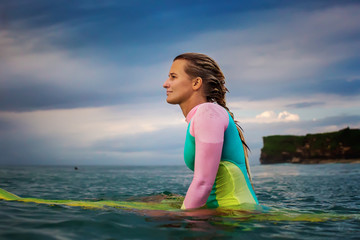 Wall Mural - surfer girl in bright swimsuit waiting for the wave in open water. sunset time at the ocean. a woman