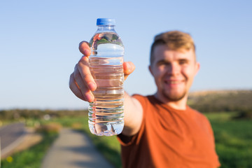 Young sporty man show bottle of water in a park