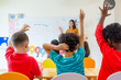 © weedezign - Preschool kid raise arm up to answer teacher question on whiteboard in classroom,Kindergarten education concept