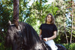 Emotional portrait of a horsewoman rider woman, astride, in love with horses, black Friesian stallion thoroughbred pet, outdoors
