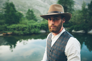 Hipster handsome male model portrait with beard wearing trendy clothes in the mountains