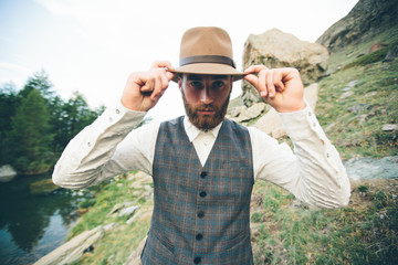 Wall Mural - Hipster handsome male model portrait with beard wearing trendy clothes in the mountains