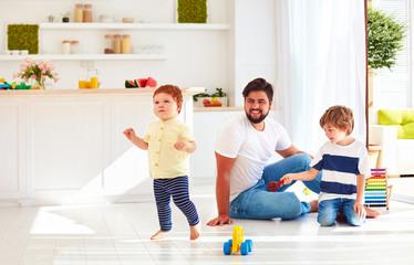 Wall Mural - happy toddler baby playing with father and brother at home at sunny summer day