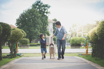 father and son walking with a siberian husky don in the park