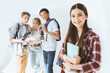 © LIGHTFIELD STUDIOS - smiling teenage girl with notebook in hands looking at camera with multicultural students behind isolated on white