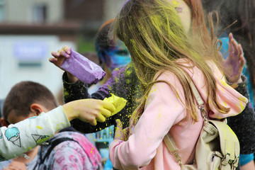 Wall Mural - Girl pours dry yellow powdery paint on her friend at the festival of Holi festival in Gatchina, Russia.