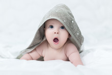 Surprised Baby Girl Or Boy After Shower With Towel On Head In White Sunny Bedroom. Child With Big Blue Eyes Open Mouth And Crying In Bed After Bath Or Shower