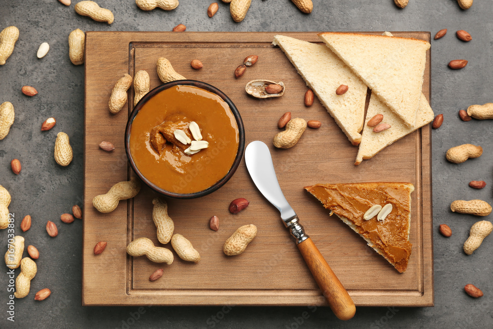 Wooden board with delicious peanut butter, toasts and nuts on table