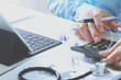 © everythingpossible - Healthcare costs and fees concept.Hand of smart doctor used a calculator for medical costs in modern hospital