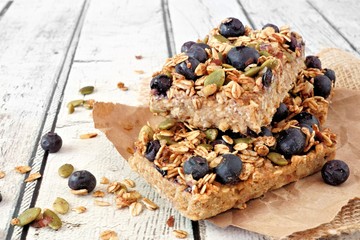 Wall Mural - Two stacked superfood breakfast bars with oats and blueberries, side view on rustic white wood