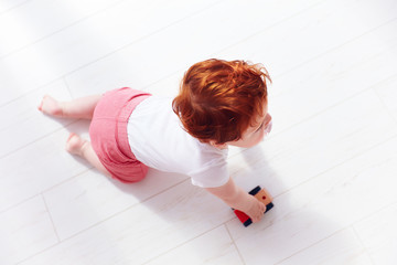 Wall Mural - top view of redhead baby boy rolling a toy car on the floor