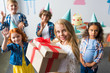 © LIGHTFIELD STUDIOS - adorable smiling girl holding birthday presents while friends waving hands