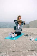 Wall Mural - Young woman exercising with senior woman by sea pier