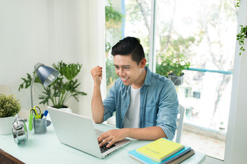 Portrait of excited asian young business man working on laptop computer at office desk