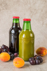  Two glass bottles with natural fruit juice, fresh apricots and grapes on a gray background. The concept of a healthy diet.