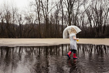 Side View Of Girl Carrying Umbrella While Walking On Puddle During Rainy Season