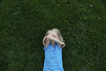 Overhead View Of Girl Covering Face While Lying On Grassy Field