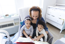 High Angle View Of Mother Reading Storybook For Daughters At Home