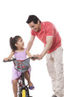 © IndiaPix - Happy father teaching daughter to ride bicycle against white background