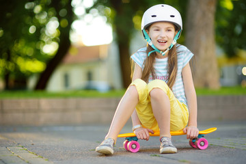 Wall Mural - Pretty little girl learning to skateboard on beautiful summer day in a park. Child enjoying skateboarding ride outdoors.