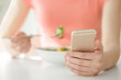 Young woman using mobile phone for counting calories while eating, closeup. Weight loss concept