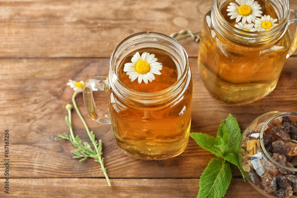 Mason jars with chamomile tea on wooden background