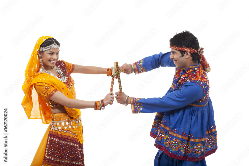 Side view of happy couple performing Dandiya Raas against white ...