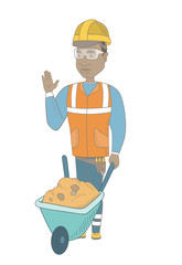 Poster - African-american builder standing near wheelbarrow full of sand. Young builder in hard hat waving his hand near wheelbarrow. Vector sketch cartoon illustration isolated on white background.