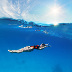 Wall Mural - Female professional swimmer swimming on back under waterline with sunshine above