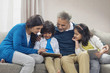 © IndiaPix - Grandchildren using digital tablet with grandparents sitting on sofa