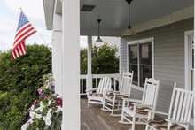USA, Bangor, Maine. A Row Of Traditional White Rocking Chairs At The Porch Of An Inn With A Stars And Stripes Flag.