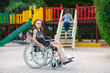 © davit85 - A girl with a broken leg sits in a wheelchair in front of the playground.
