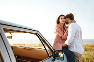 Canvas Print - Young beautiful couple embracing while leaning on a vintage car