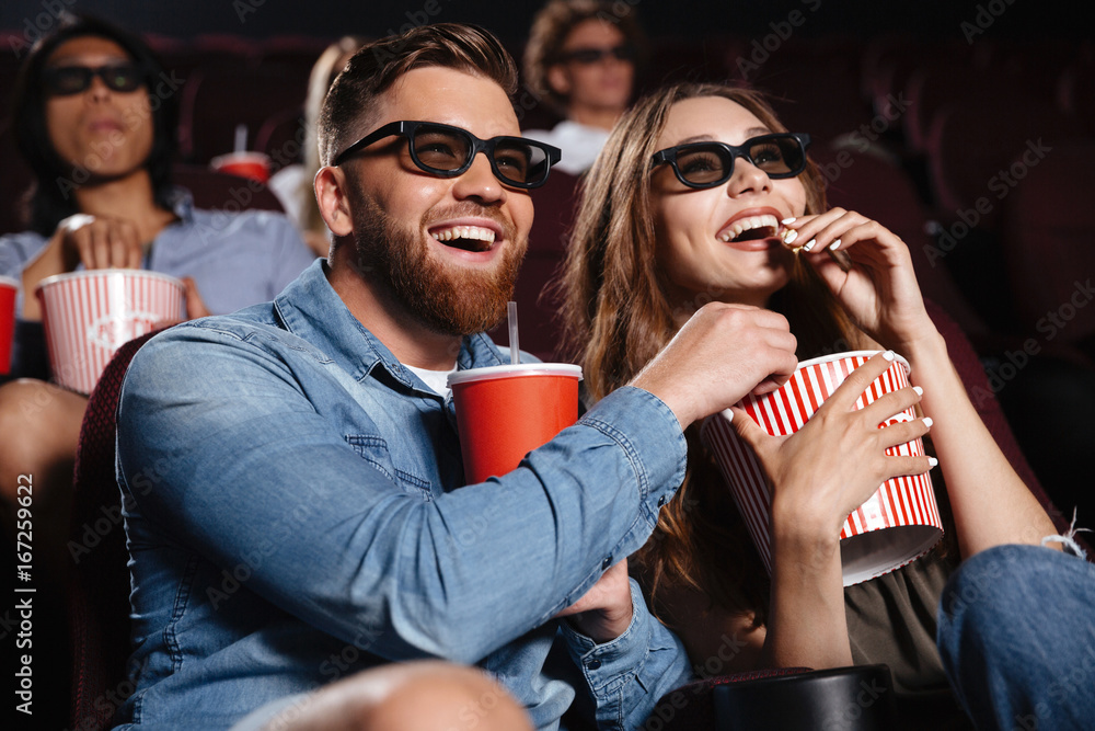Happy friends sitting in cinema watch film eating popcorn - obrazy, fototapety, plakaty 