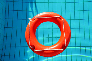 Red lifebuoy pool ring float, ring floating in refreshing blue swimming pool. Red float floating in the pool with blue water. Inflatable red swim ring floating on a pure water with sunny reflections.