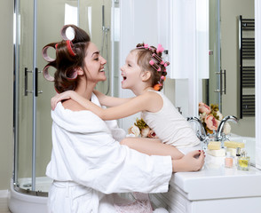 young mother and daughter in curlers in a bath room happy smiling hugging