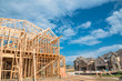 © trongnguyen - New stick built home under construction and blue sky in US. Framing structure/wood frame of wooden houses next to completed suburban home. Pile of sand, gravel, logs in front. Industrial, real estate