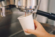 © anoushkatoronto - Closeup of young Caucasian barista hands holding paper cup making coffee using  coffee machine. Woman pouring coffee from professional espresso machine. Toned with film filters.