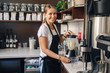 Portrait of  happy beautiful young Caucasian smiling woman barista preparing smoothie with ice. Server making cold drink in coffee shop. Toned with film filters.